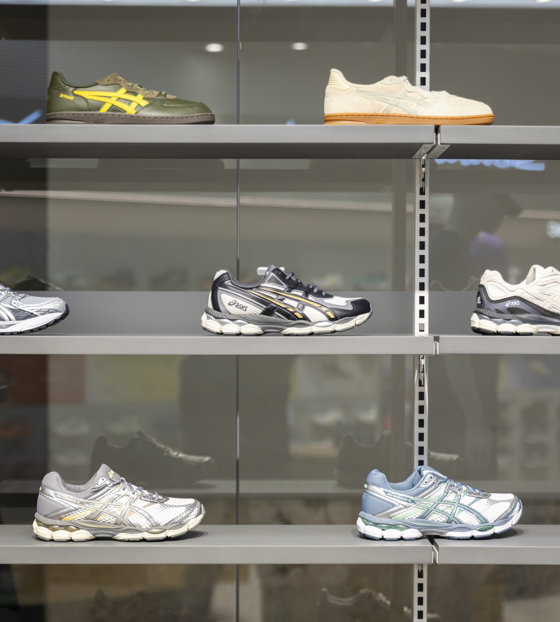 Asics sneakers lined up across the glass-fronted shelving of a Frontera-operated store.
